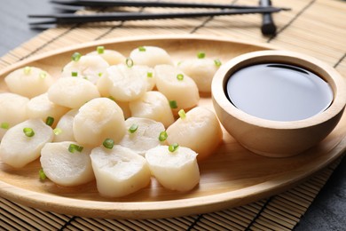 Photo of Raw scallops with green onion and soy sauce on dark table, closeup