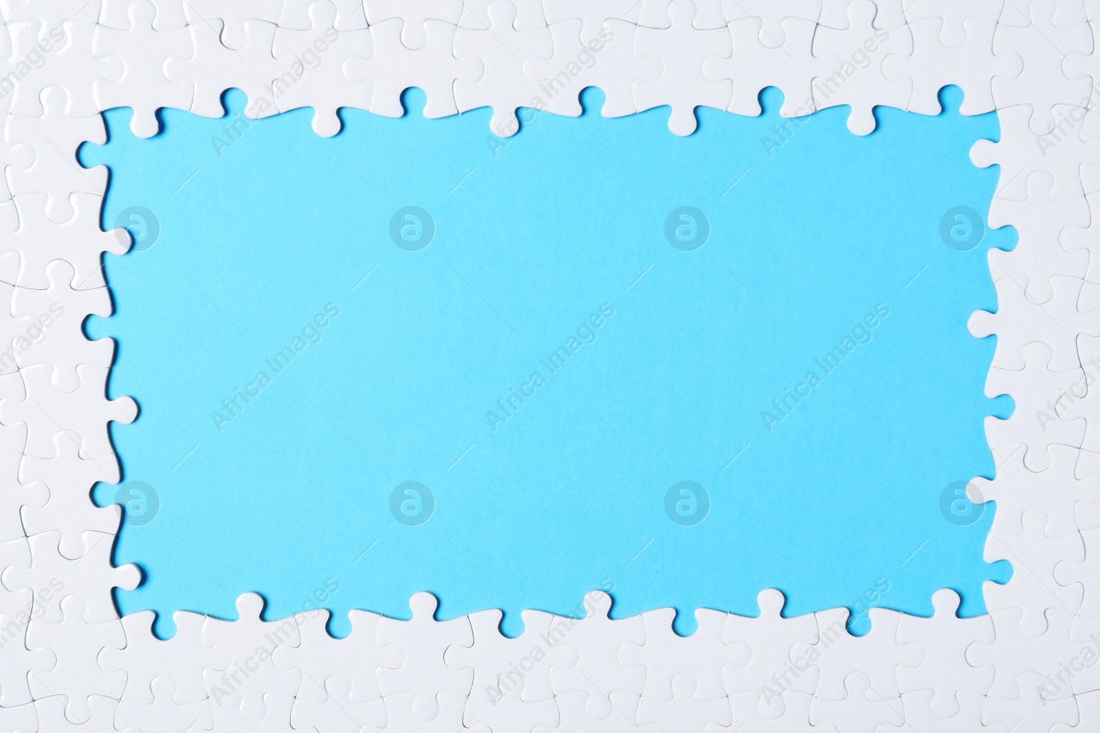 Photo of Frame made with white puzzle pieces on light blue background, top view. Space for text