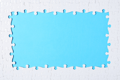 Photo of Frame made with white puzzle pieces on light blue background, top view. Space for text