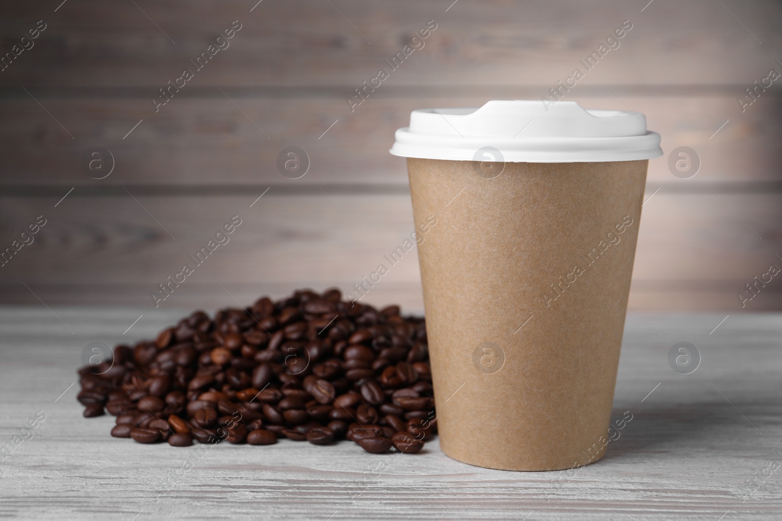 Photo of Coffee to go. Paper cup and roasted beans on light wooden table, space for text