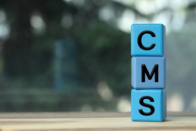 Abbreviation CMS of blue cubes on wooden table against blurred background, space for text. Content management system