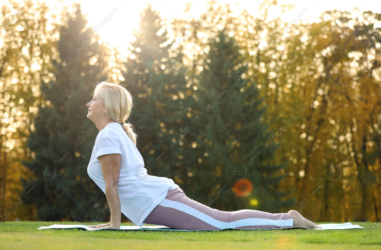 Image of Mature woman practicing yoga on green grass in park