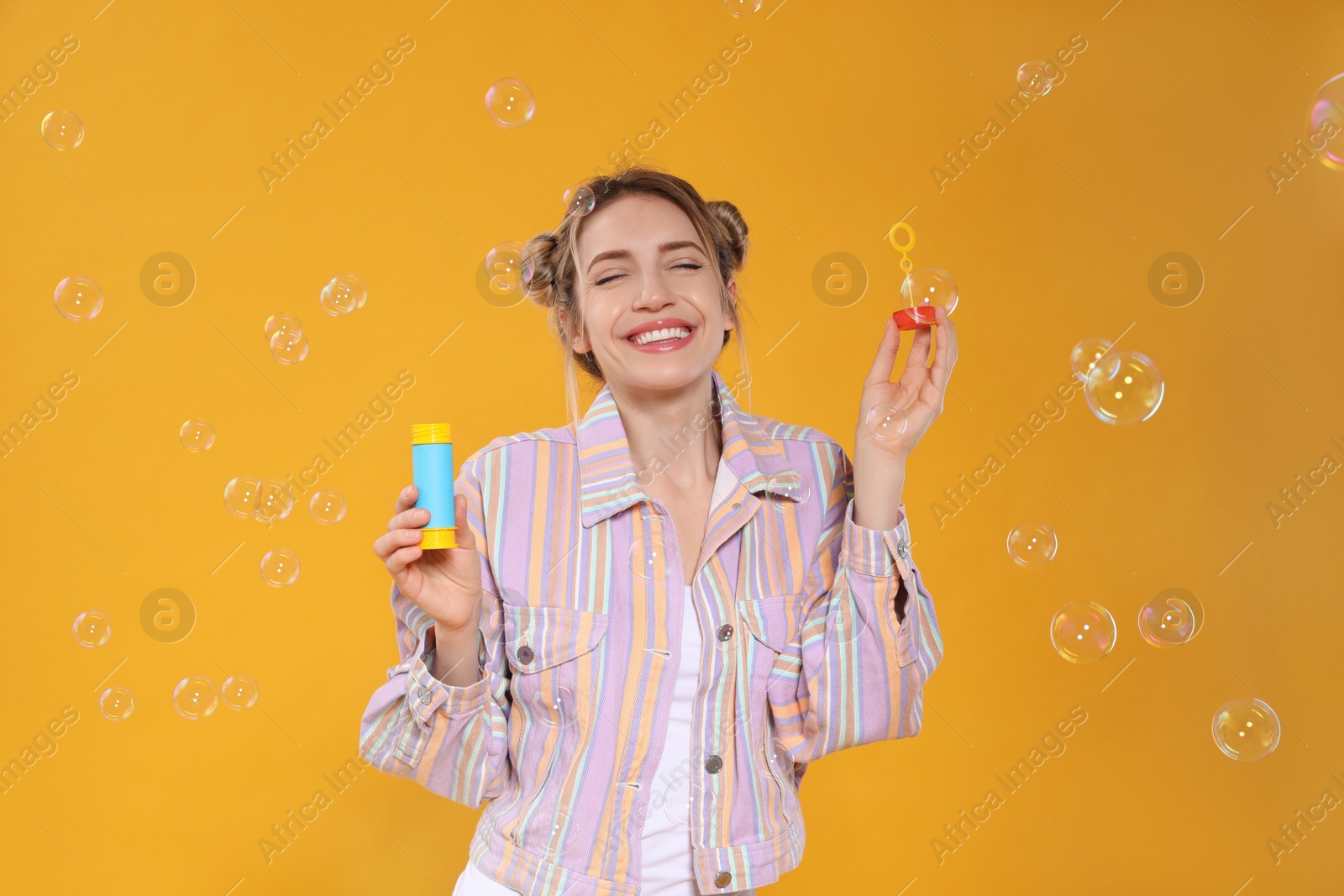 Photo of Young woman blowing soap bubbles on yellow background