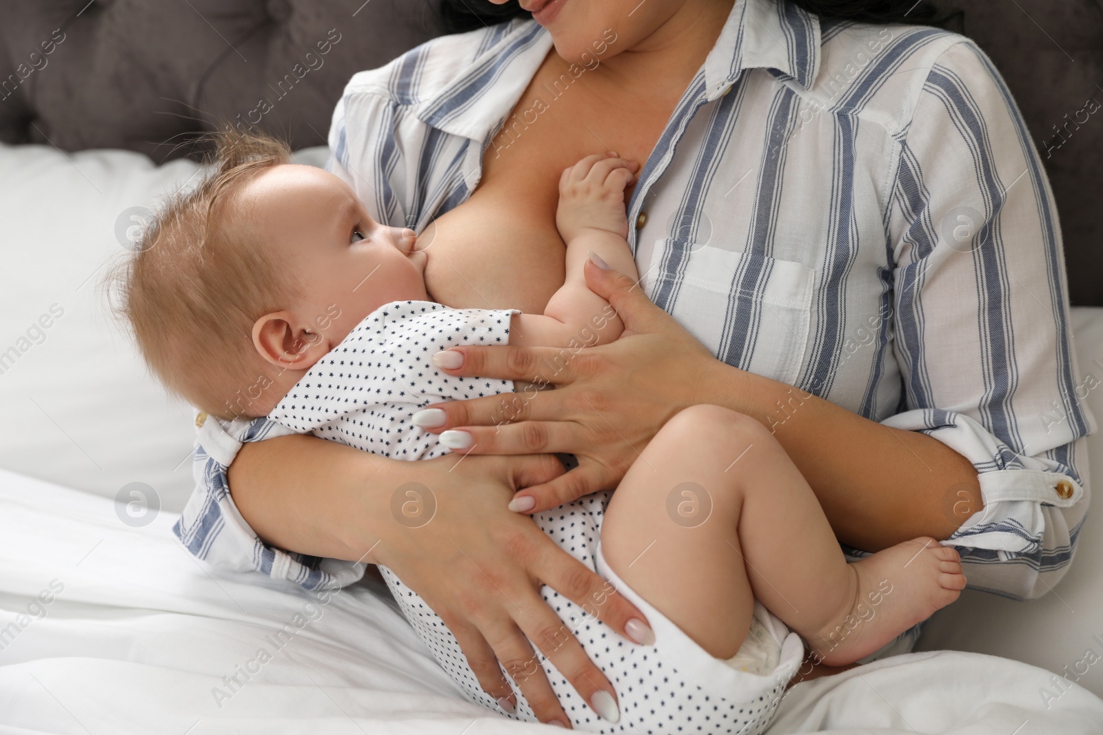 Photo of Woman breastfeeding her little baby on bed indoors