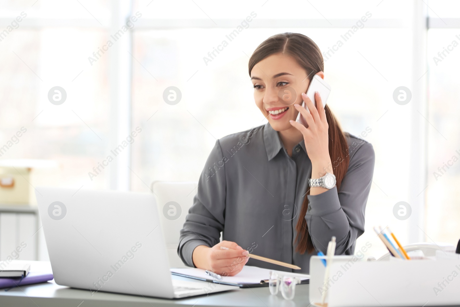 Photo of Young woman talking on phone at workplace