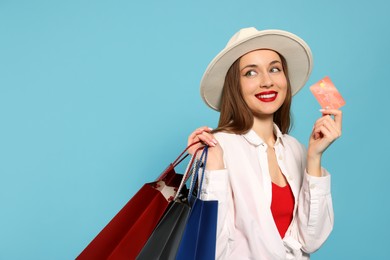 Photo of Stylish young woman with shopping bags and credit card on light blue background, space for text