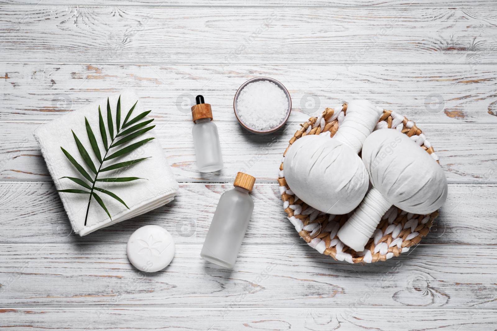 Photo of Beautiful spa composition with herbal massage bags and different care products on white wooden table, flat lay