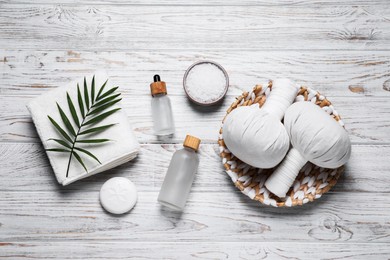 Beautiful spa composition with herbal massage bags and different care products on white wooden table, flat lay