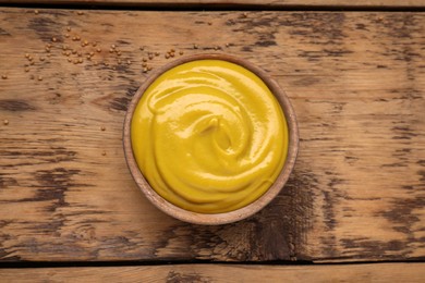 Photo of Sauce bowl with delicious mustard and seeds on wooden table, top view