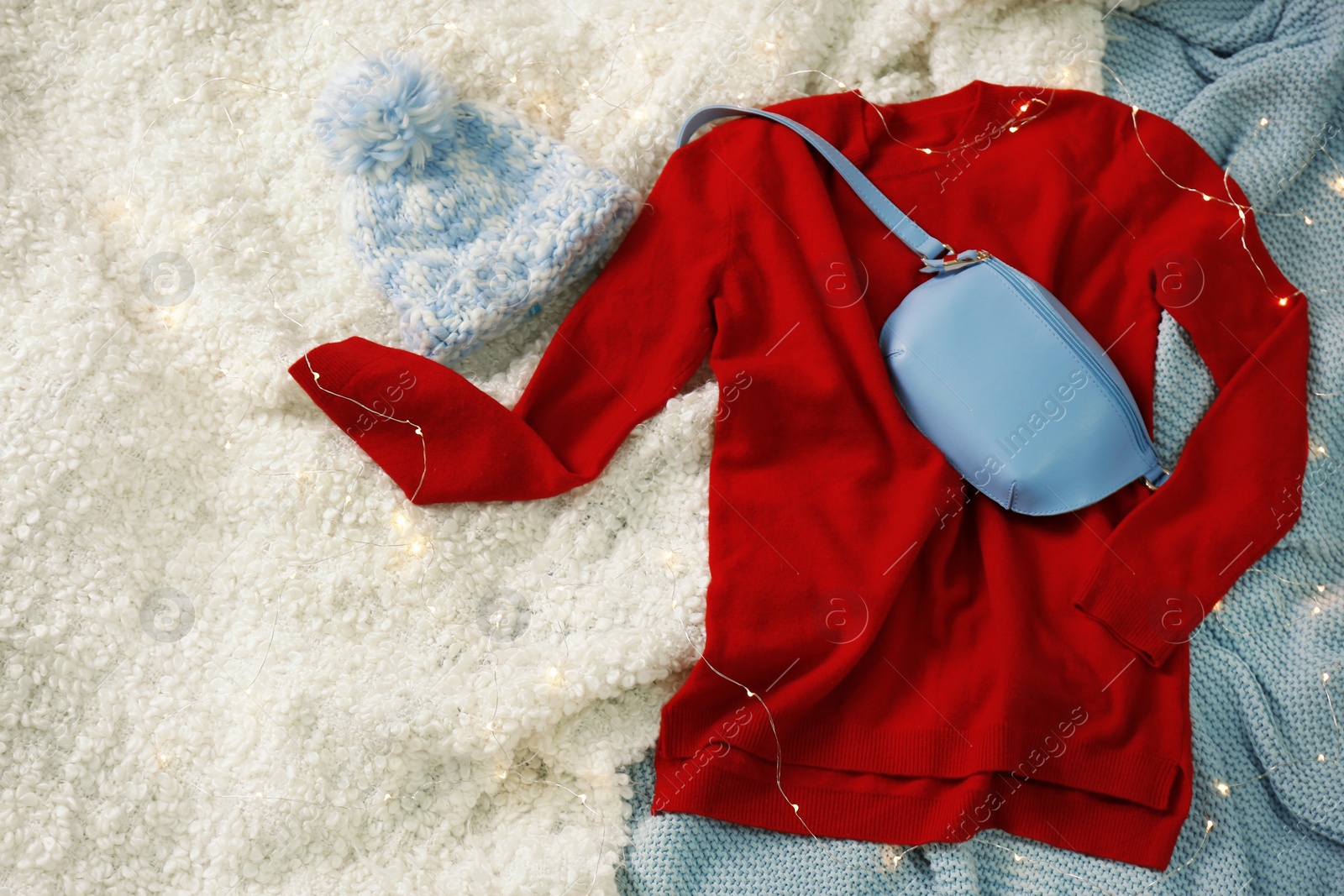 Photo of Flat lay composition with red sweater and hat on soft blankets. Space for text