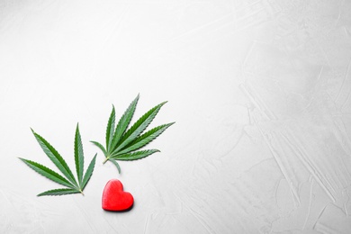 Photo of Green hemp leaves and red heart on light background, flat lay. Space for text