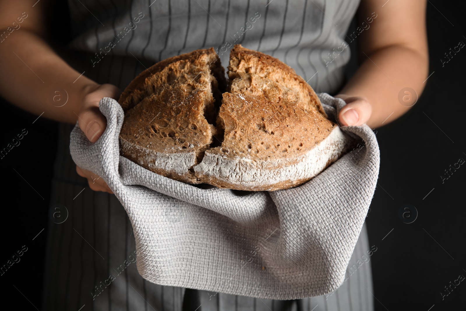 Photo of Woman holding tasty bread on dark background, closeup