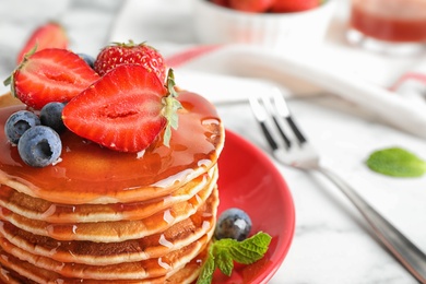 Plate of delicious pancakes with fresh berries and syrup on white marble table, closeup