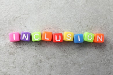 Photo of Colorful cubes with word Inclusion on light grey background, flat lay