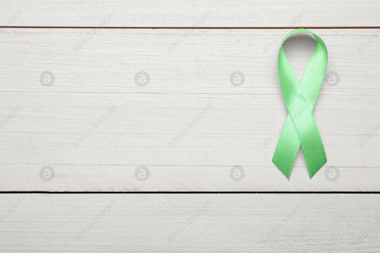 Photo of World Mental Health Day. Green ribbon on white wooden background, top view with space for text