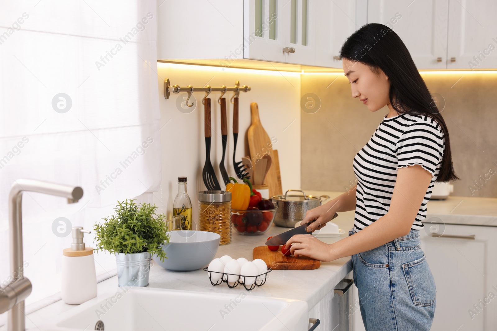 Photo of Cooking process. Beautiful woman cutting tomato in kitchen