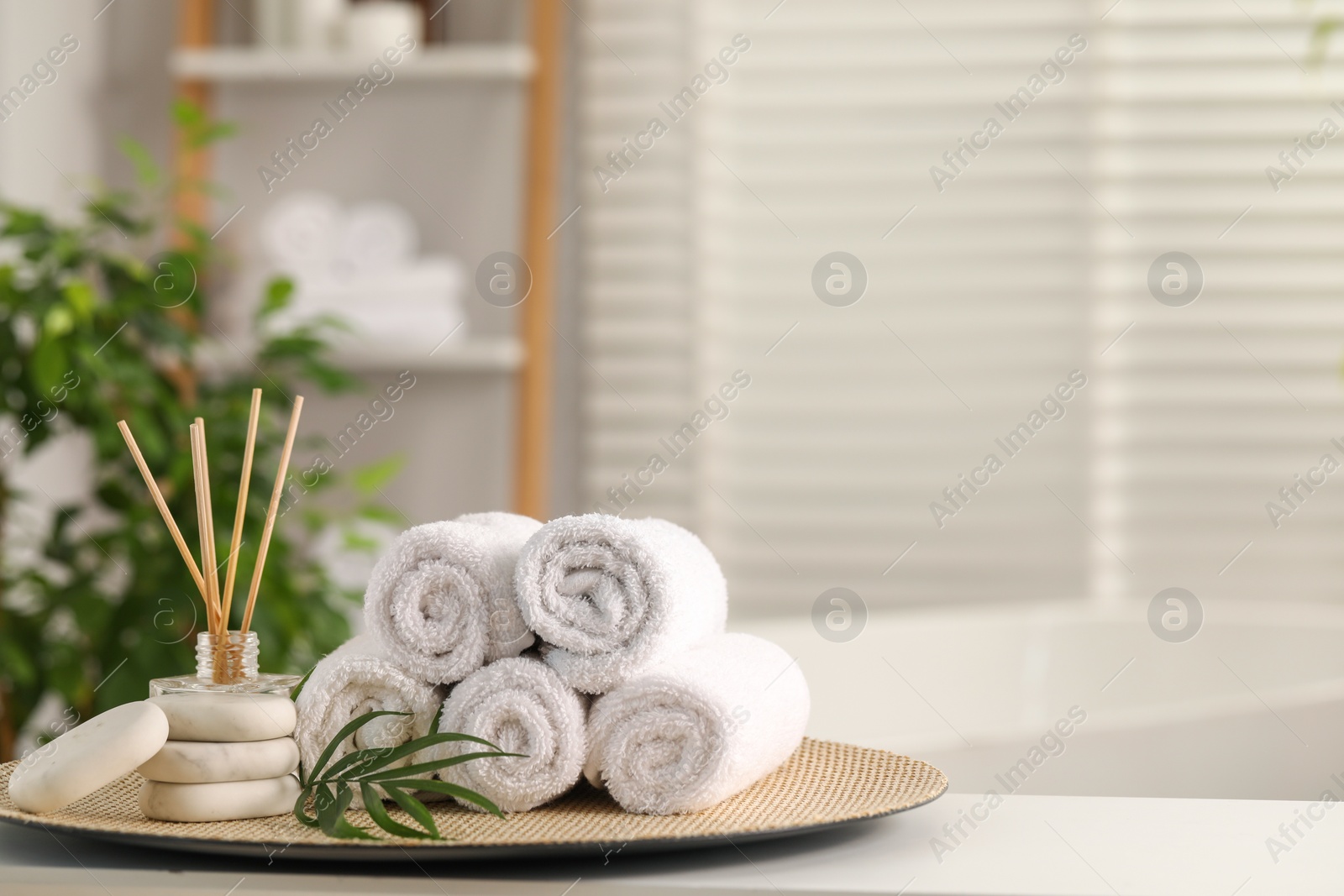 Photo of Spa composition. Towels, reed diffuser, stones and palm leaves on white table in bathroom, space for text