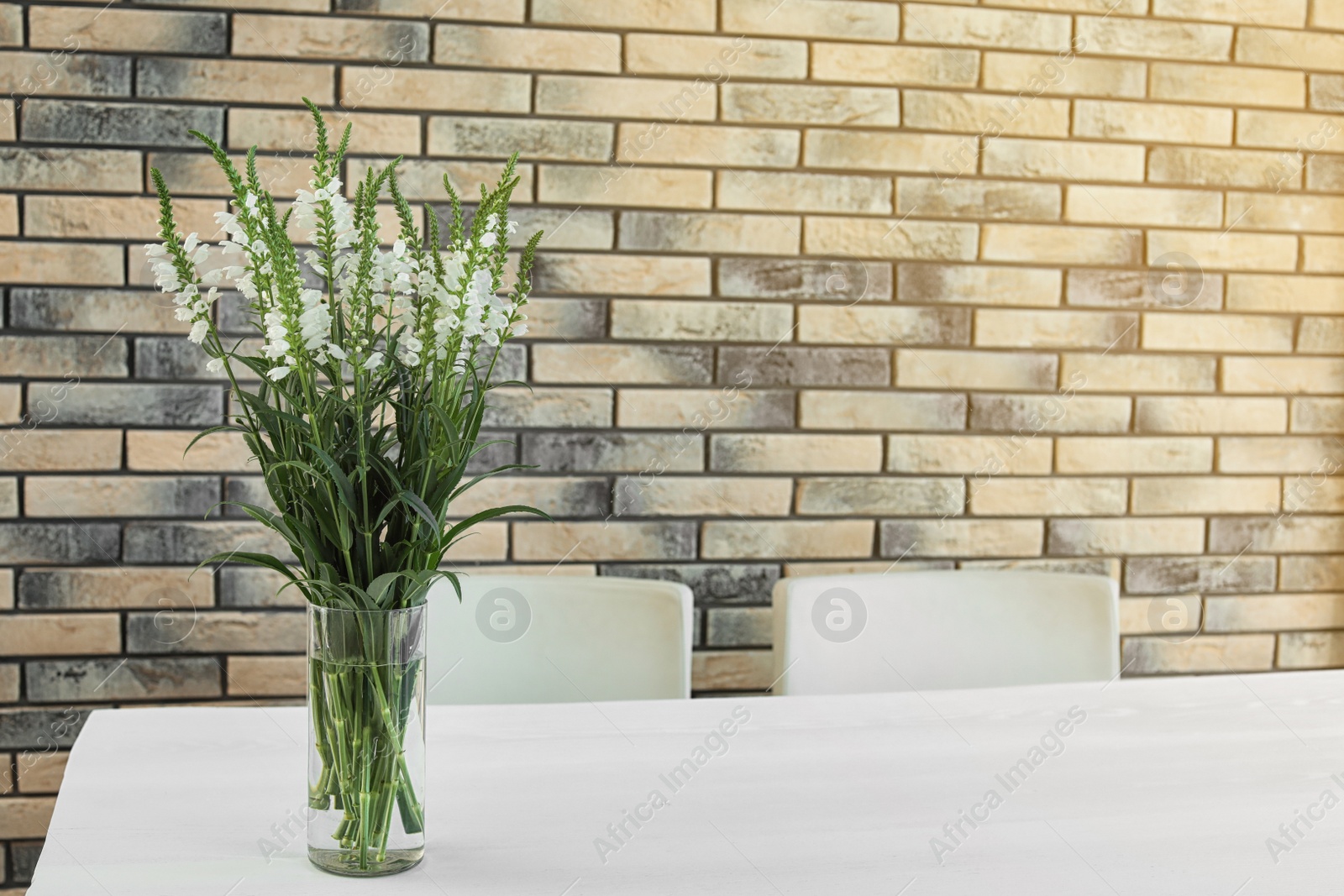 Photo of Vase with beautiful flowers on white table against brick wall. Stylish interior