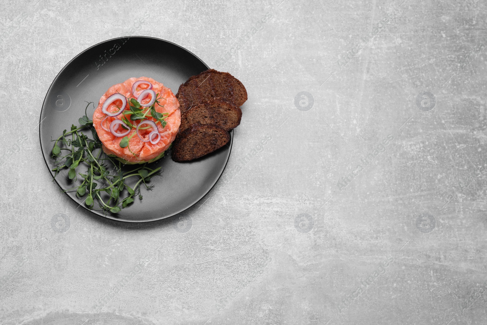 Photo of Tasty salmon tartare with microgreens and croutons on grey table, top view. Space for text