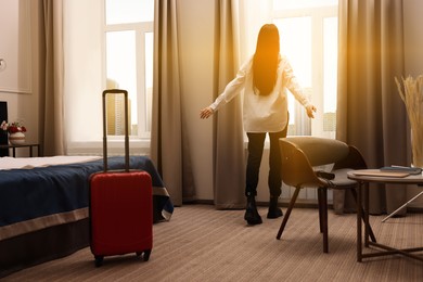 Image of Young woman near window in hotel room, back view