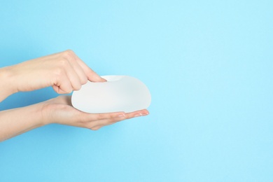 Photo of Woman touching silicone implant for breast augmentation on color background, space for text. Cosmetic surgery