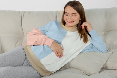 Photo of Happy pregnant woman lying on beige sofa indoors