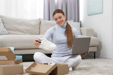Photo of Happy woman with laptop unpacking parcels at home. Online store