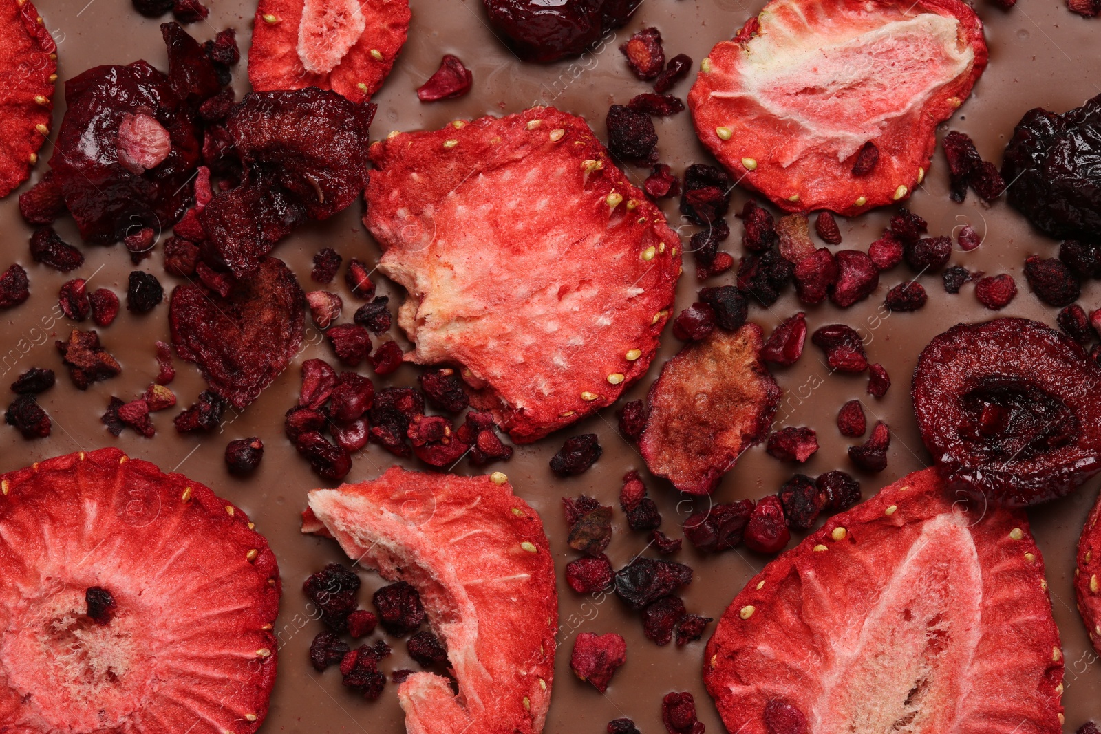 Photo of Chocolate bar with freeze dried strawberries and cherries as background, closeup