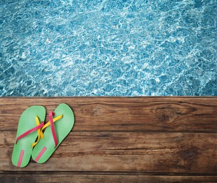 Image of Pair of flip flops on wooden deck near swimming pool, top view  