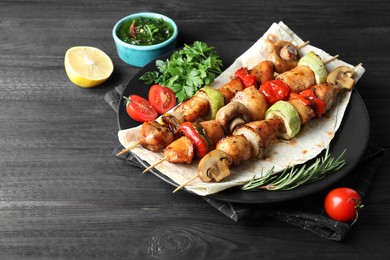 Photo of Delicious shish kebabs with vegetables served on black wooden table, closeup
