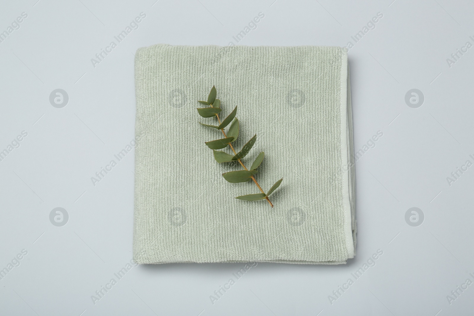 Photo of Soft green towel and eucalyptus branch on light grey background, top view