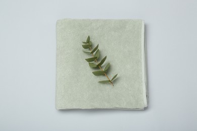 Photo of Soft green towel and eucalyptus branch on light grey background, top view