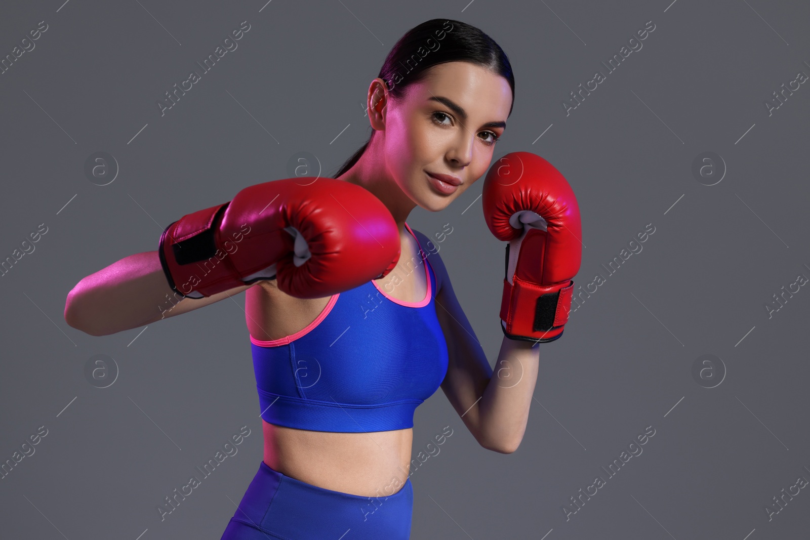 Photo of Portrait of beautiful woman wearing boxing gloves in color lights on grey background