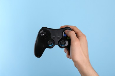 Man using wireless game controller on light blue background, closeup