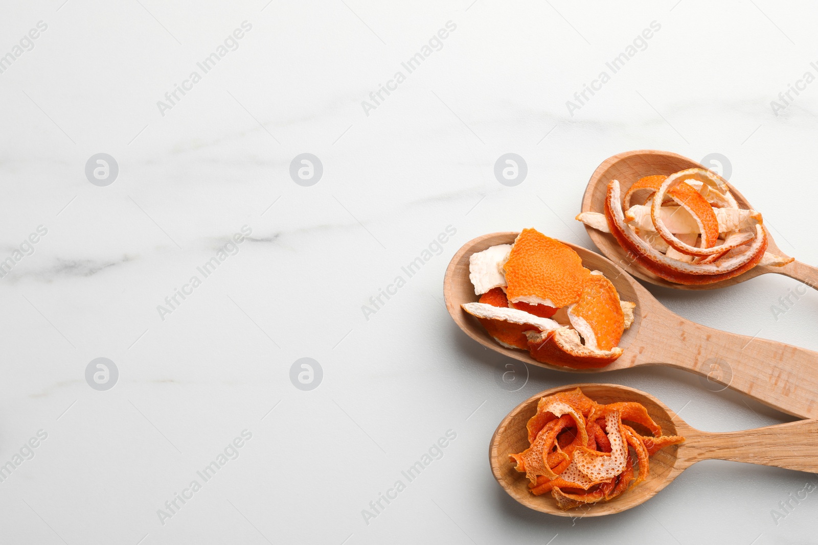 Photo of Spoons with dry orange peels on white marble table, flat lay. Space for text