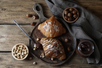 Photo of Delicious croissants with chocolate and nuts on wooden table, flat lay