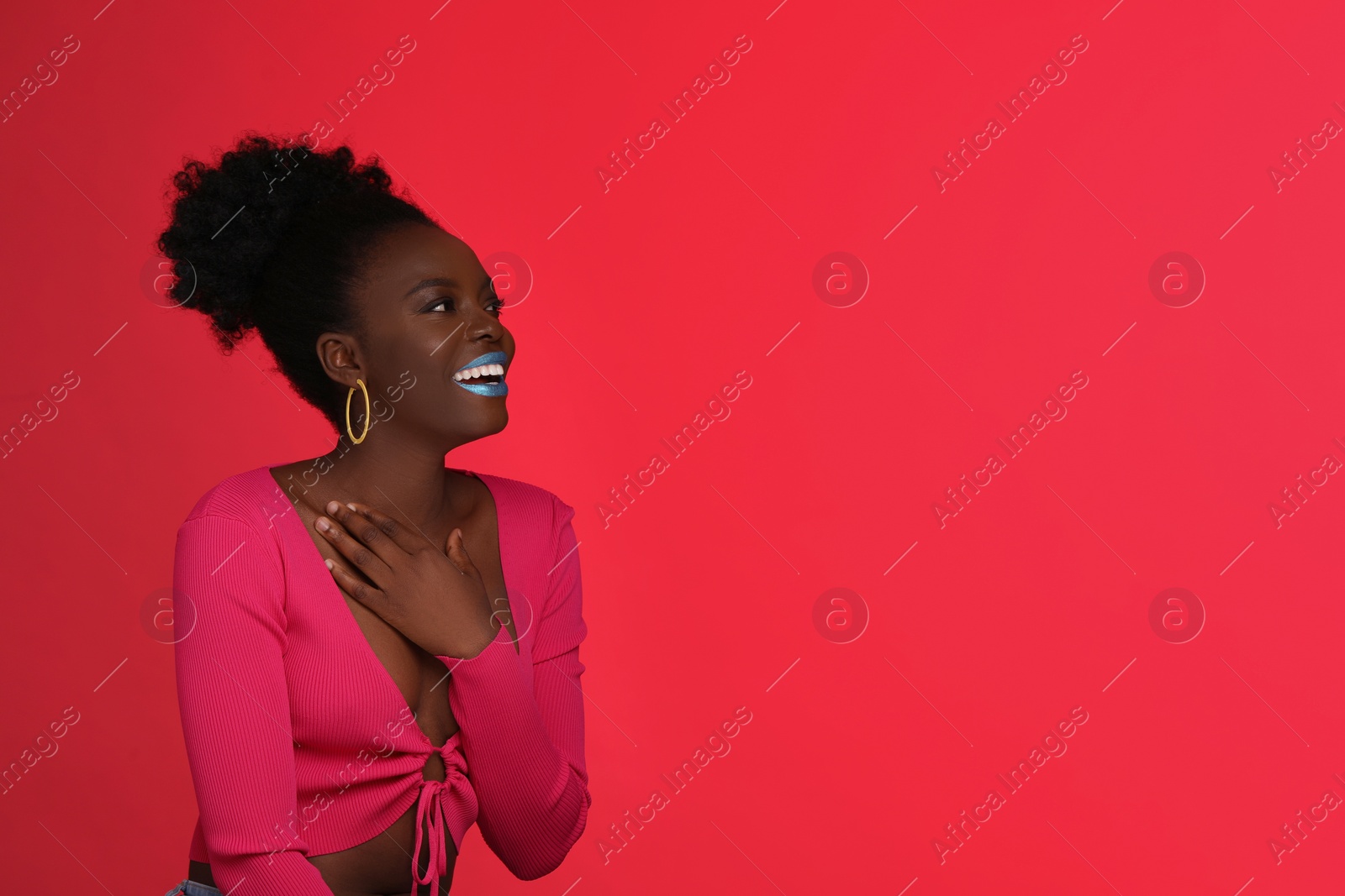 Photo of Fashionable portrait of beautiful happy woman with bright makeup on coral background, space for text