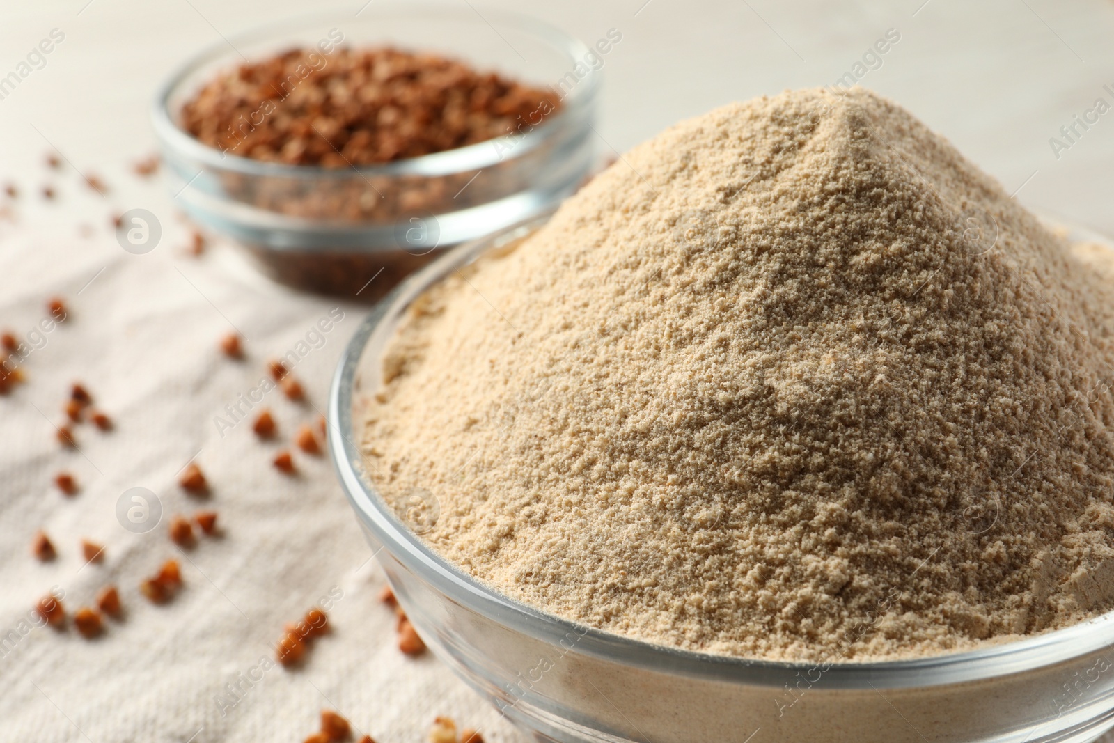 Photo of Glass bowl of buckwheat flour and cloth on white table, closeup