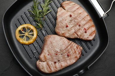 Photo of Delicious tuna steaks with lemon and rosemary on black table, top view