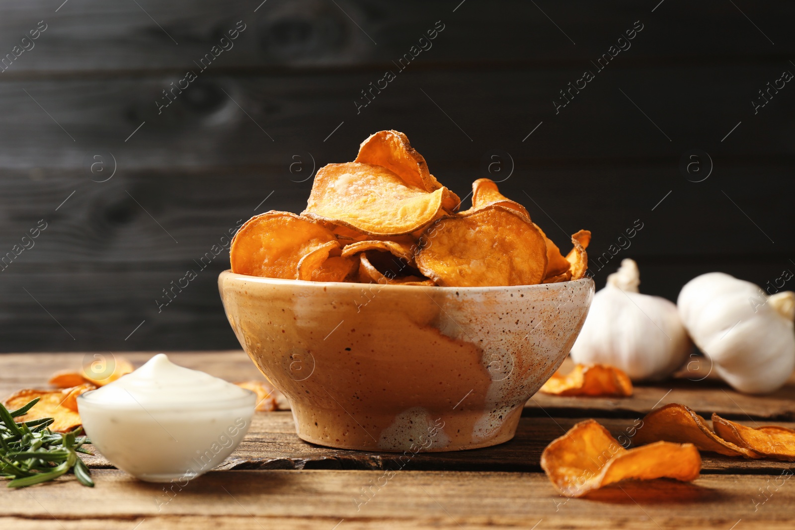 Photo of Delicious sweet potato chips in bowl, rosemary and sauce on table