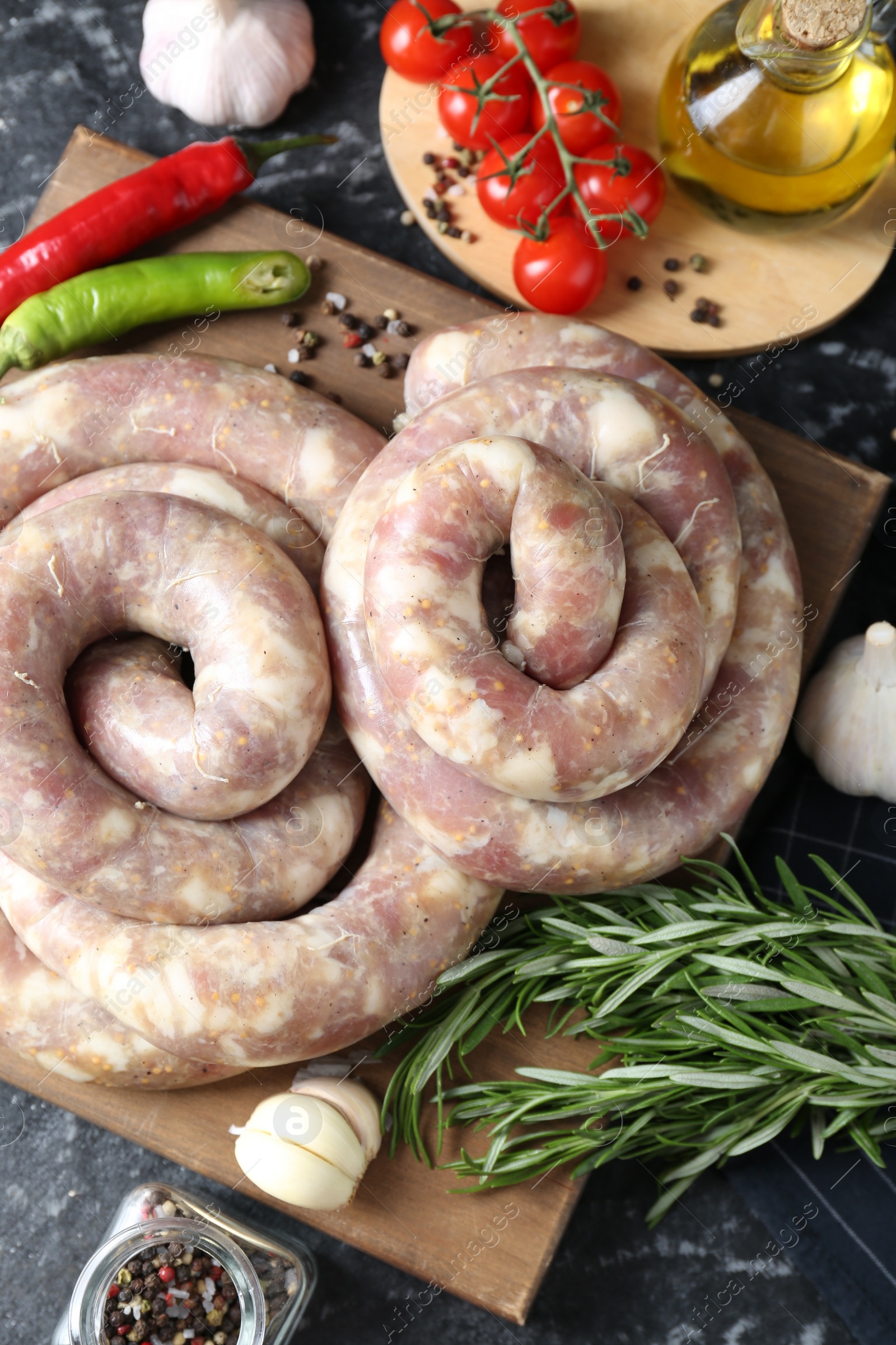 Photo of Raw homemade sausage, spices and other products on grey textured table, flat lay