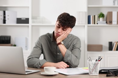 Photo of Tired young man working at table in office. Deadline concept