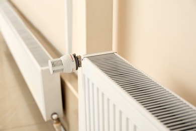 Photo of Heating radiator with thermostat near light wall indoors