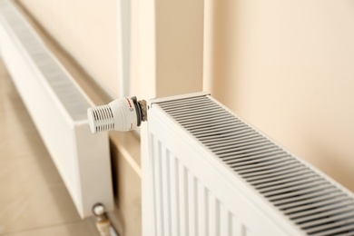 Heating radiator with thermostat near light wall indoors