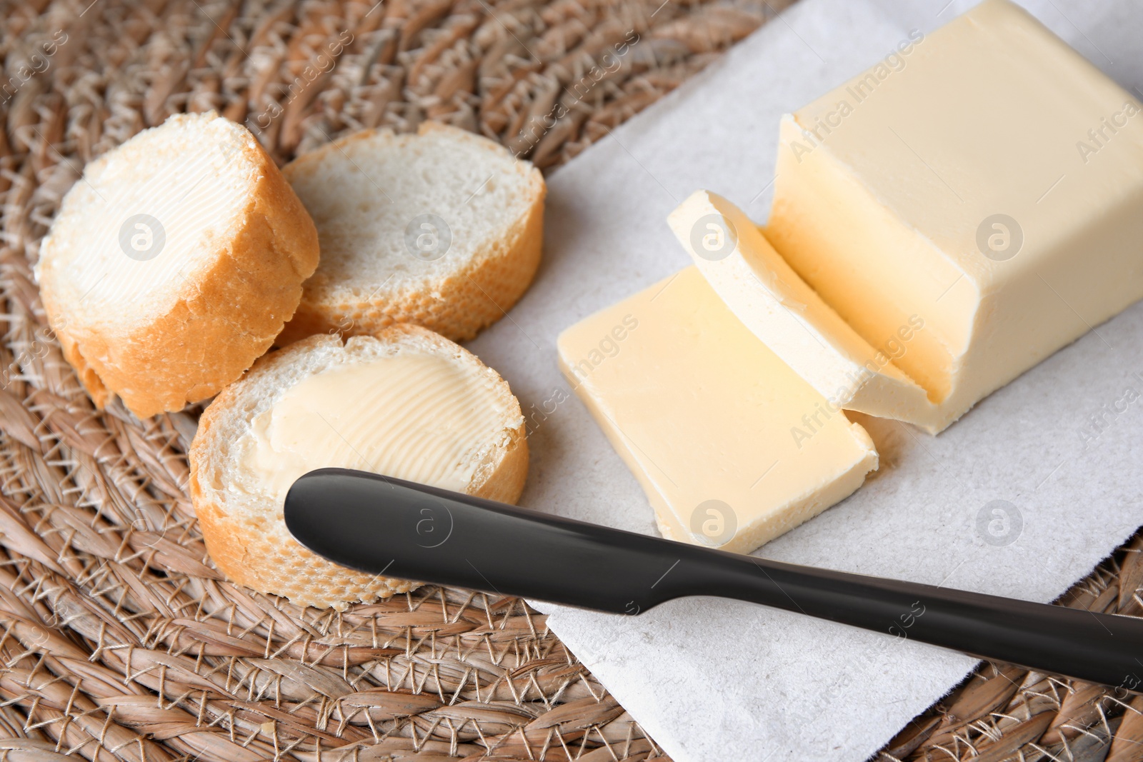 Photo of Tasty cut baguette with fresh butter on wicker mat, closeup