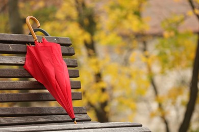 Red umbrella on bench in autumn park, space for text