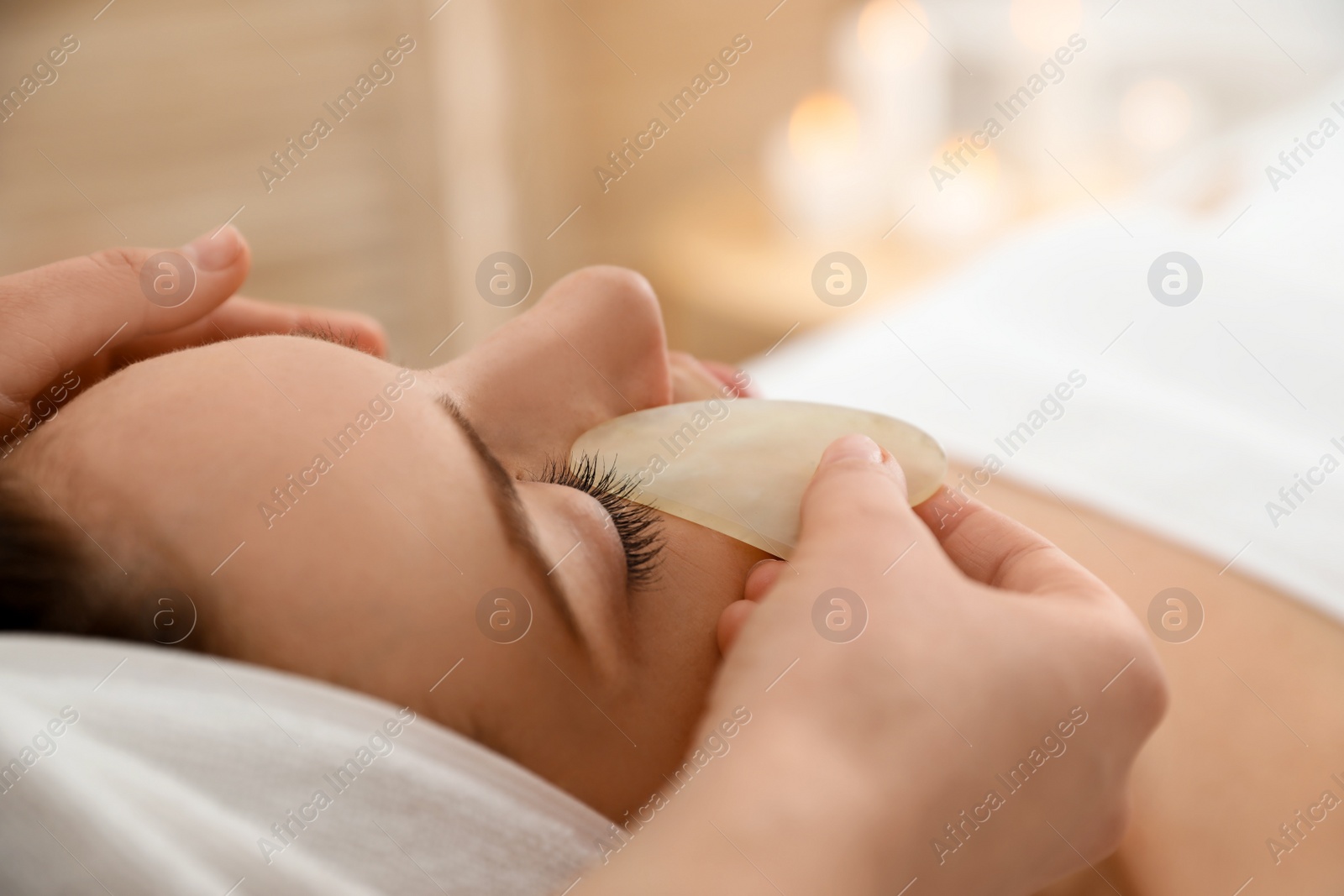 Photo of Young woman receiving facial massage with gua sha tool in beauty salon, closeup