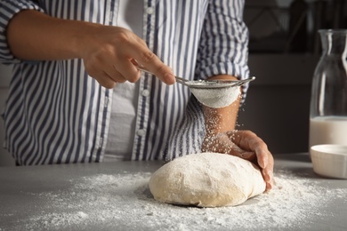 Photo of Woman sprinkling dough for pastry with flour on table