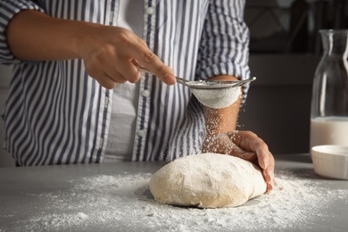 Woman sprinkling dough for pastry with flour on table