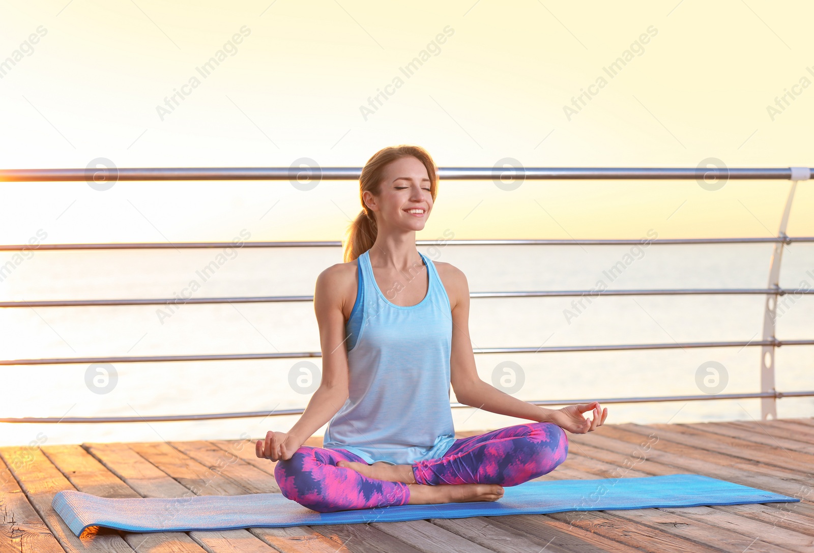 Photo of Young woman doing yoga exercises on pier in morning